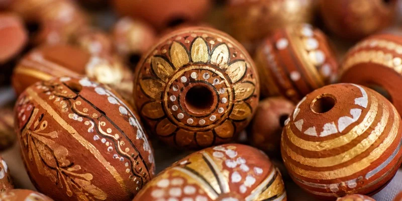 Close-up macro shot of hand-painted terracotta clay beads, intricate patterns, warm earthy red and gold tones